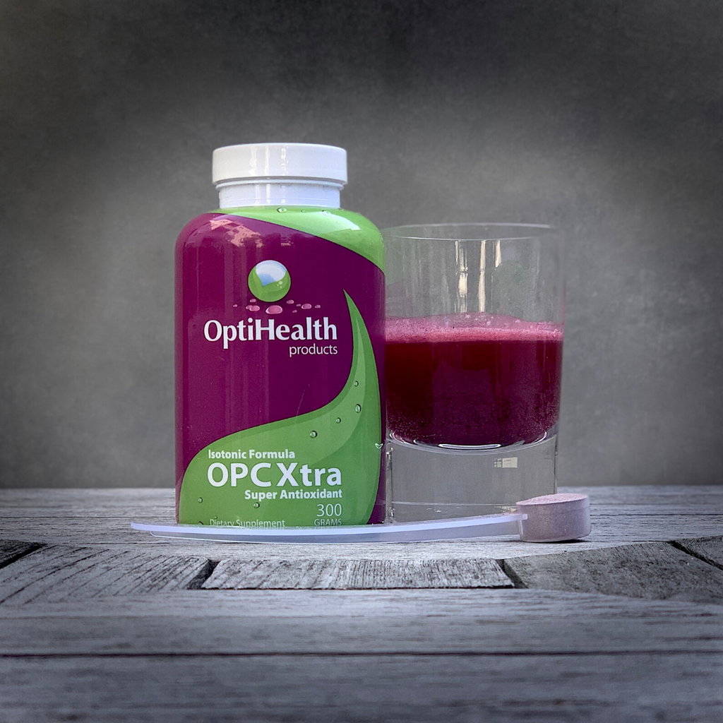 A supplement bottle beside a glass of purple liquid and a scoop on wooden surface.